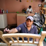 Fernando stains a piece of furniture as his mother, Eustoquia, cleans laundry behind him. The family's house sits directly above the store front and the workshop.